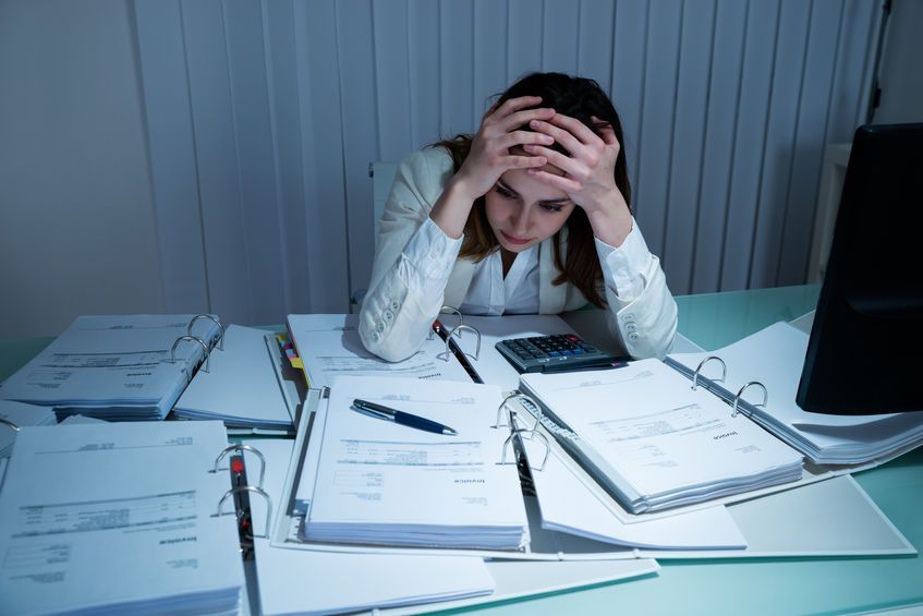 A woman is sitting at a desk surrounded by papers and a calculator.