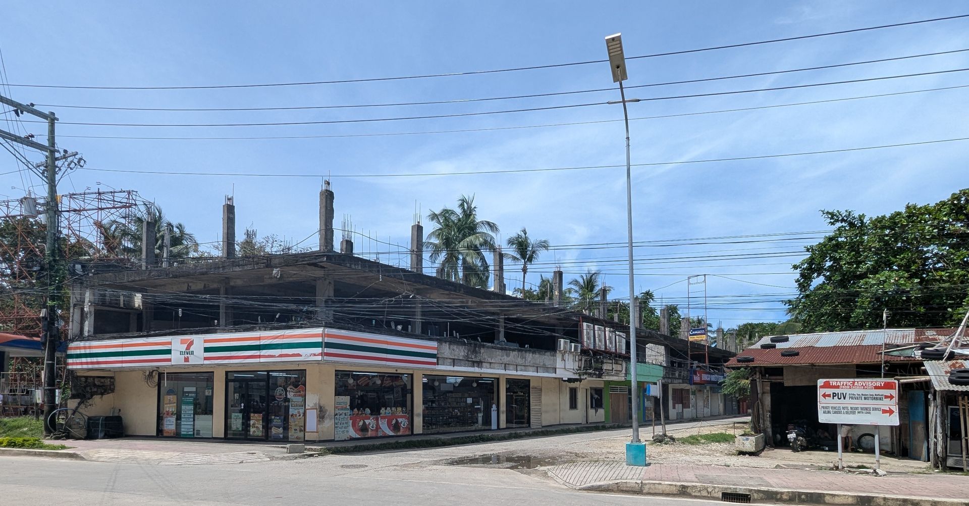 A damaged 7-Eleven store with a burned second story, located on a street under a bright, clear sky.