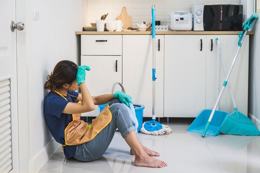 A woman is sitting on the floor in a kitchen with a mop and bucket.