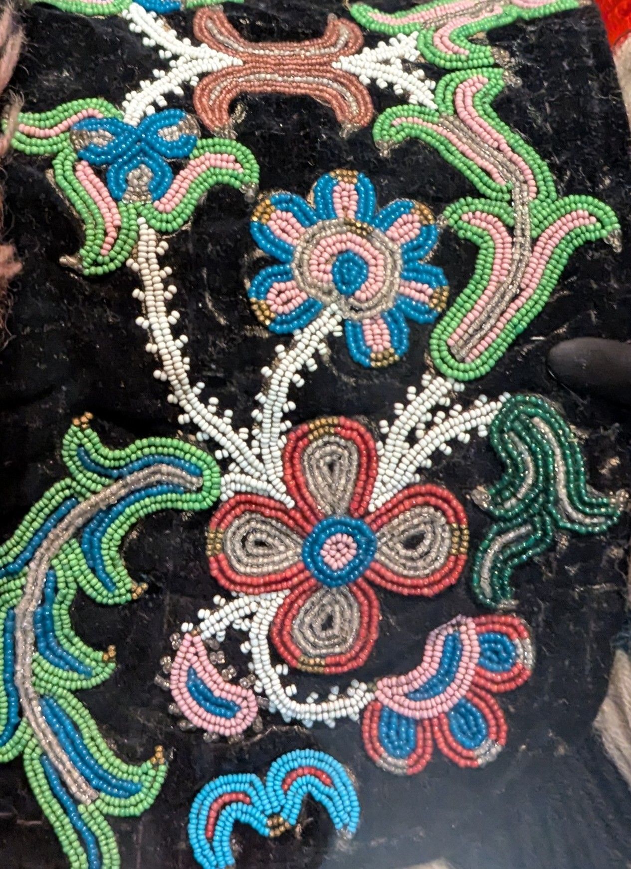 Close-up of beaded floral embroidery on black fabric, featuring various colorful flowers and leaves.