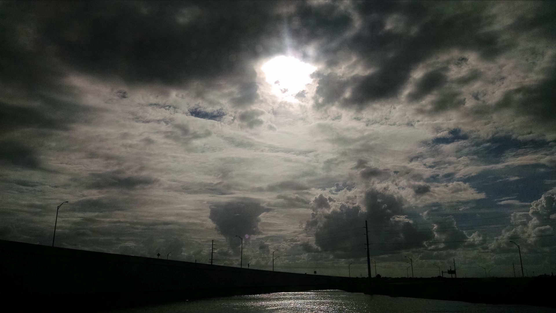 The sun is shining through the clouds over a body of water.