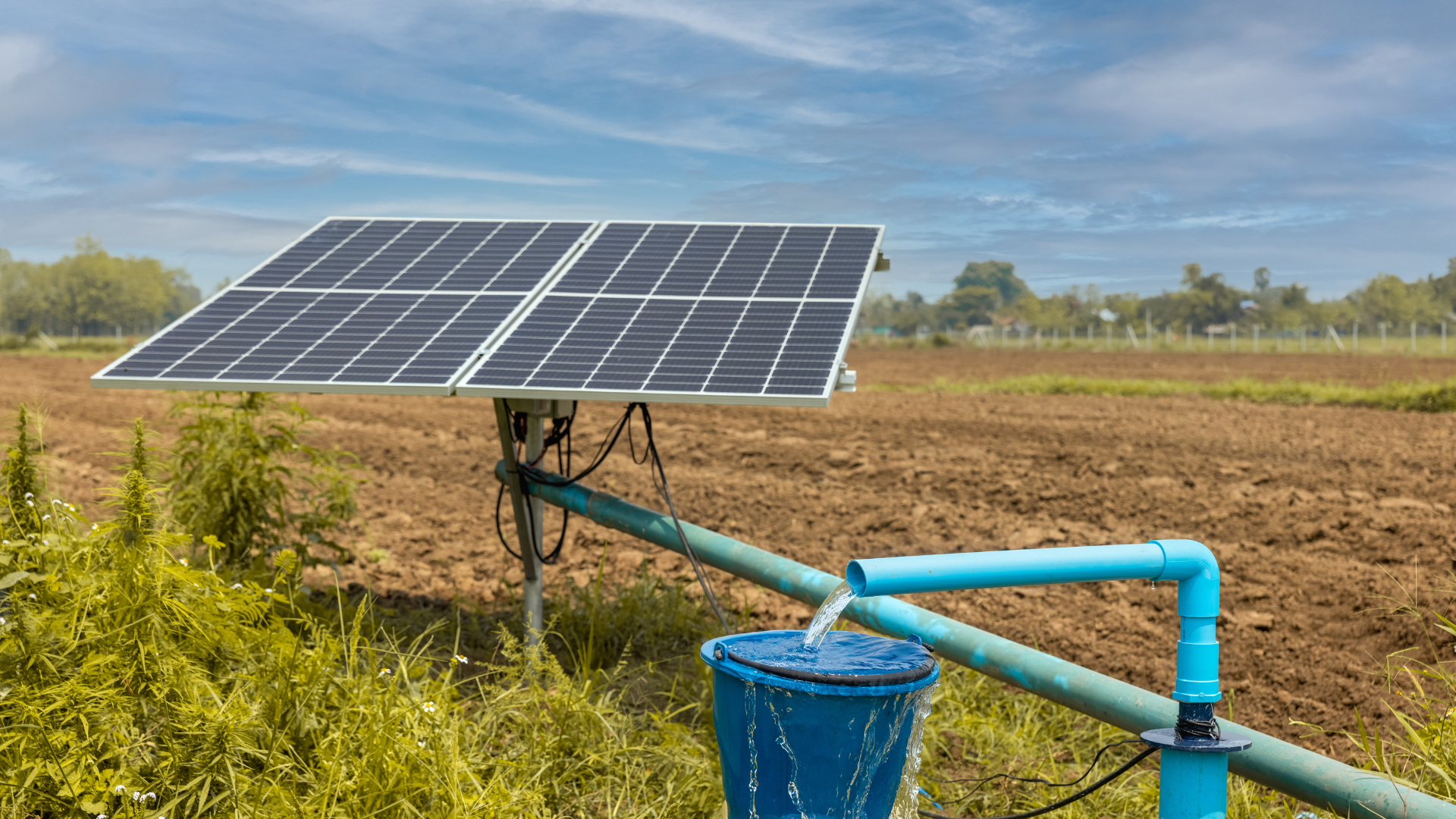 A solar panel is sitting next to a water pump in a field.