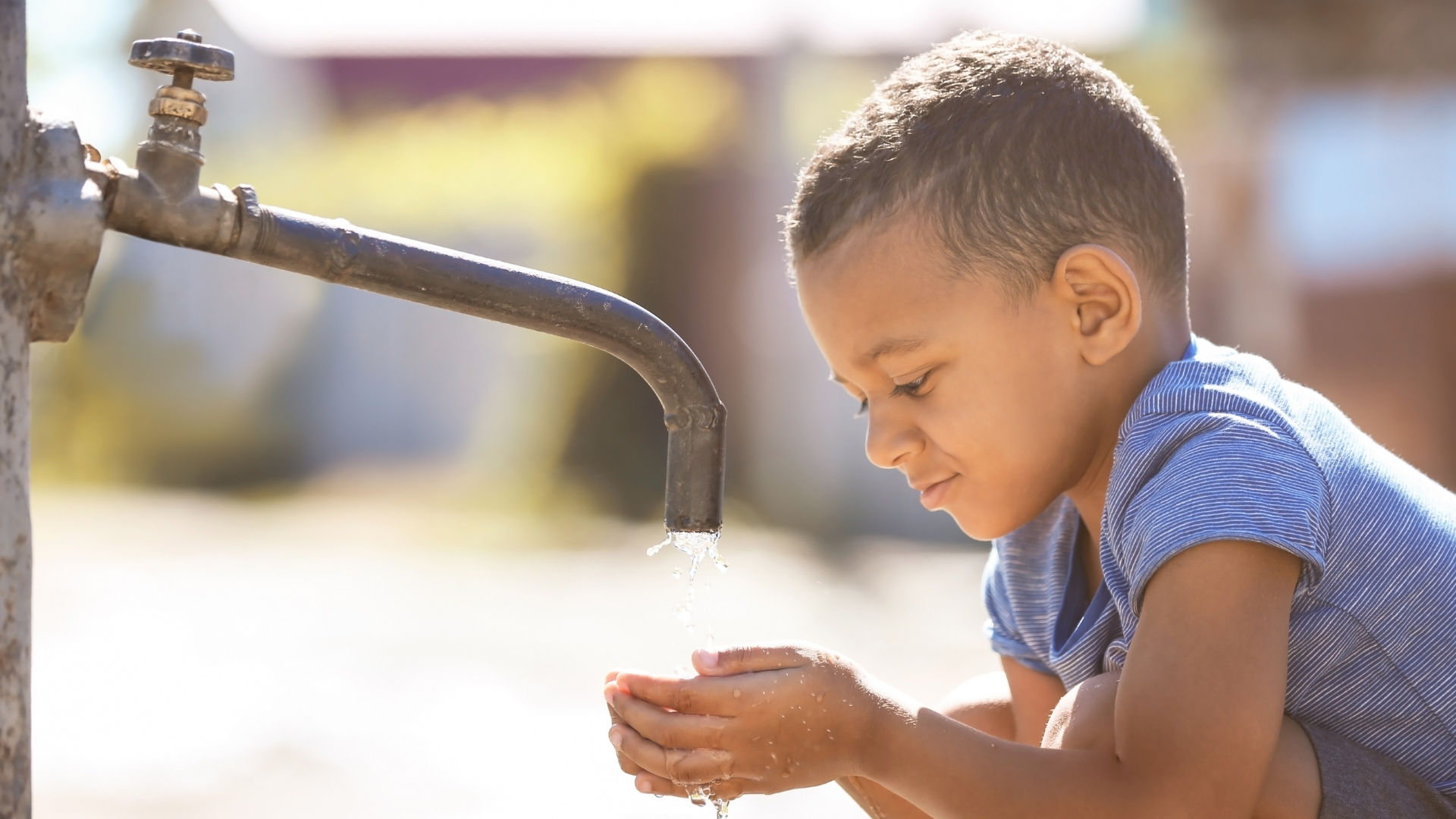 A young boy is washing his hands at a water fountain.