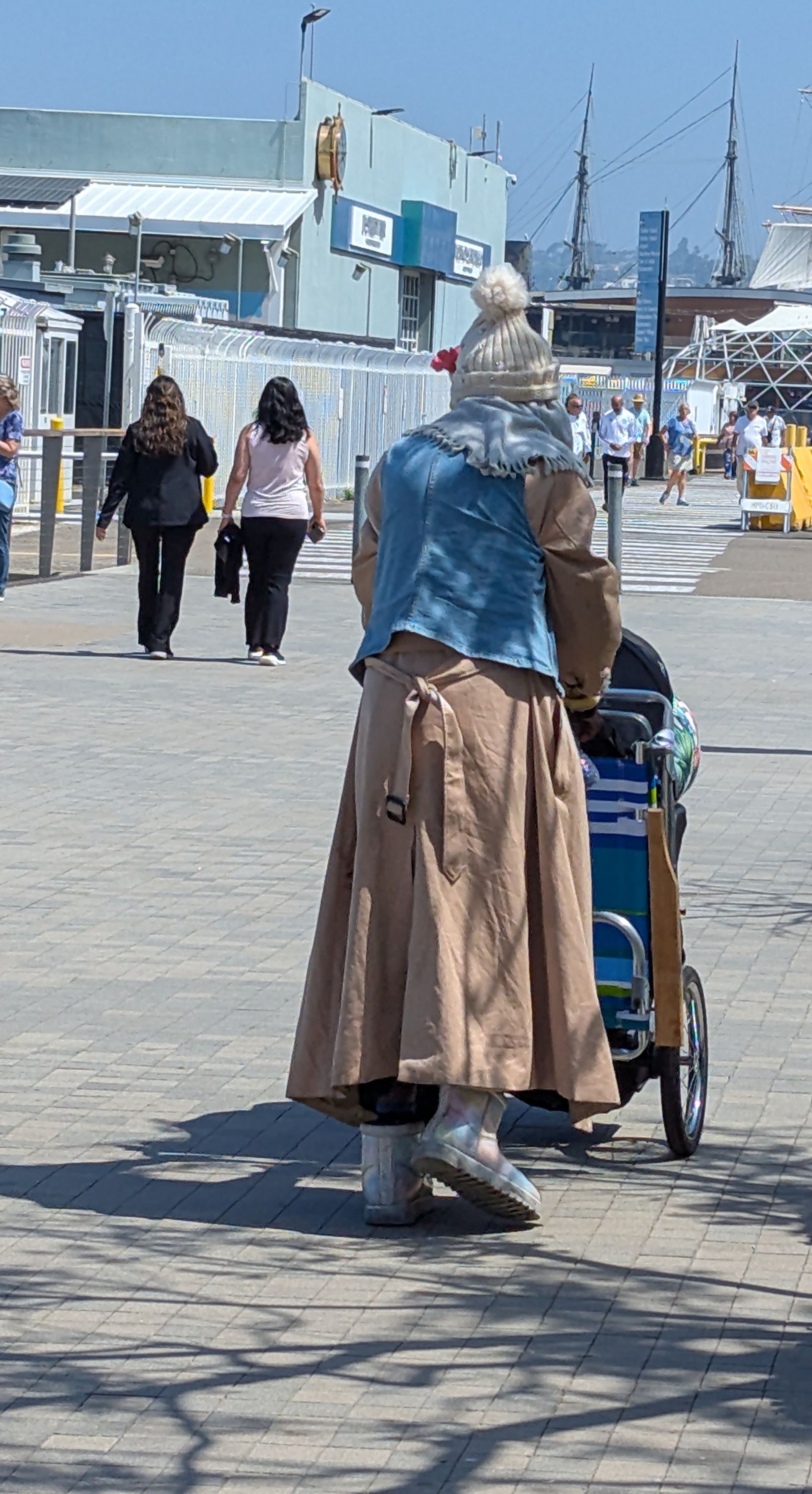 A woman pushing a wheelchair down a sidewalk with people walking behind her.