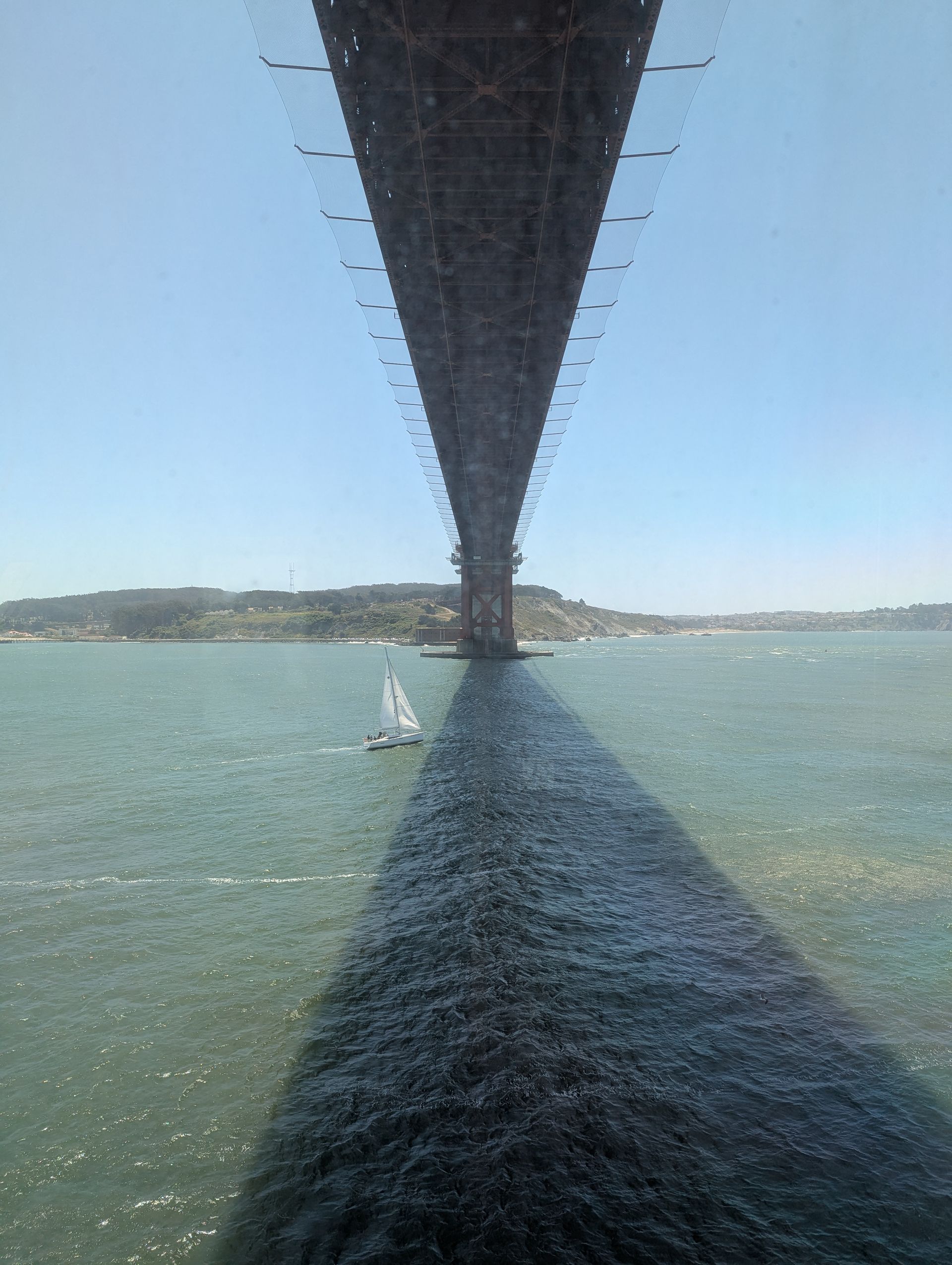 A sailboat is under a bridge over a body of water.