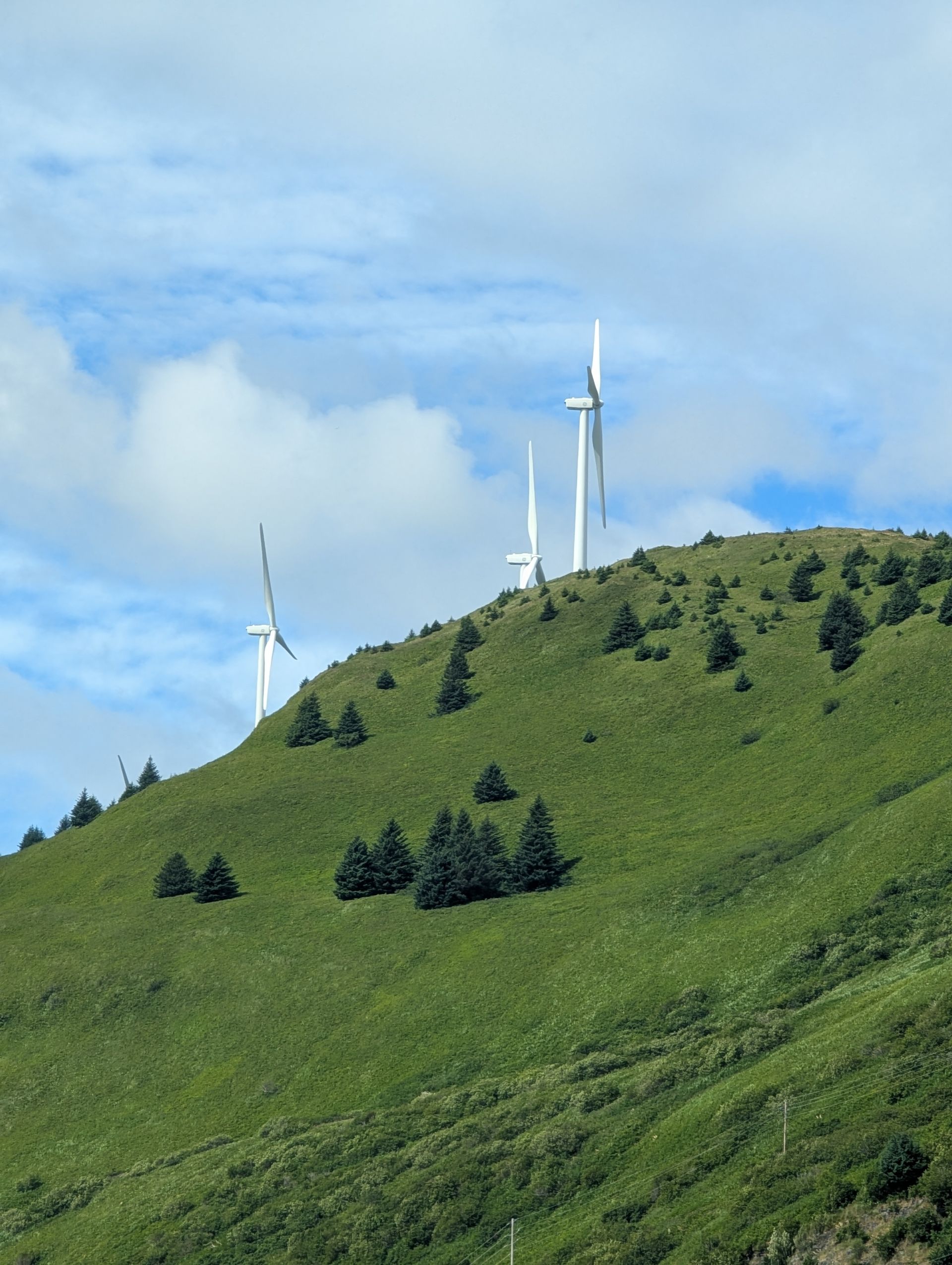 Wind turbines on a green hillside under a partly cloudy blue sky.