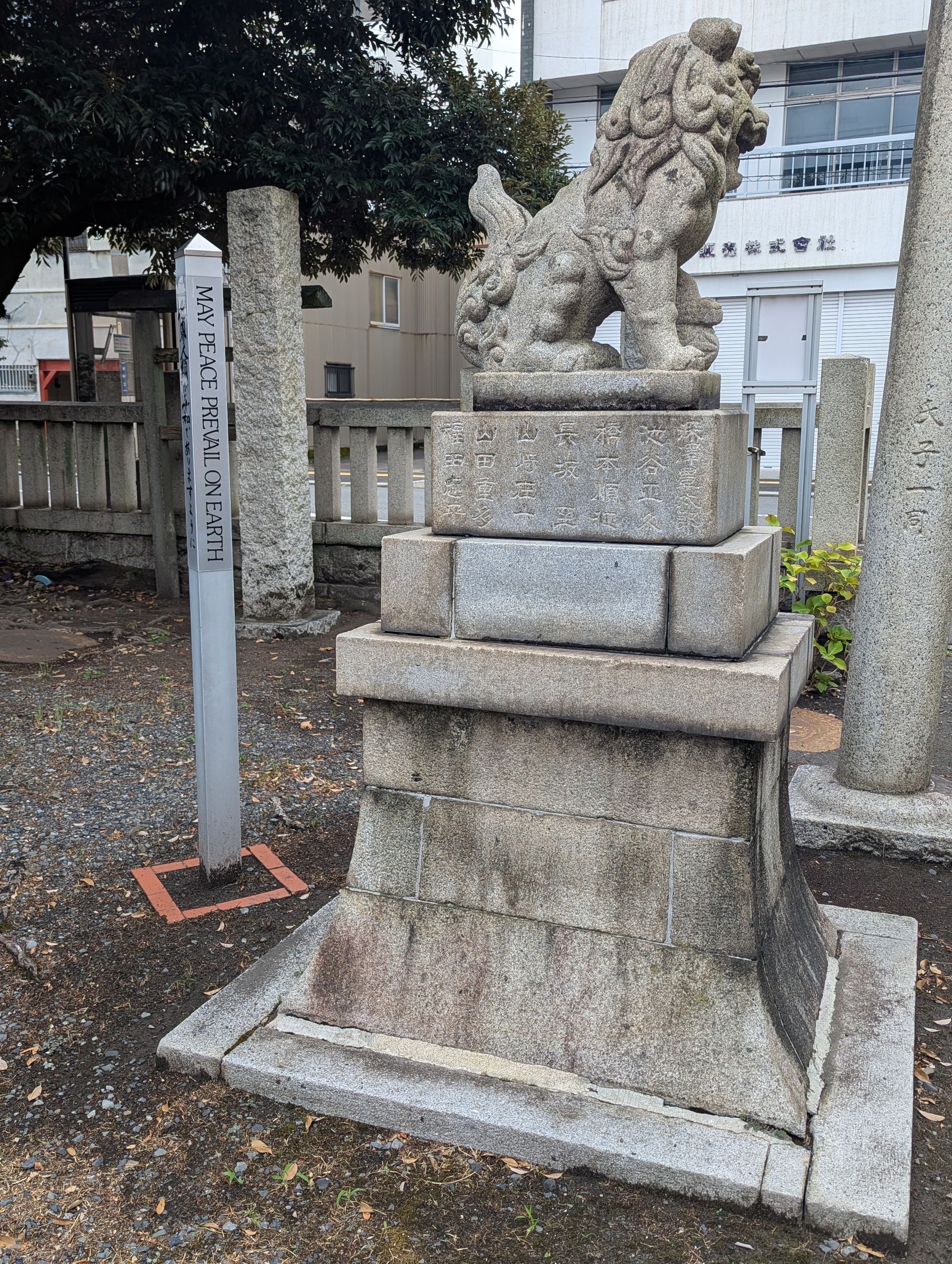 Stone komainu (lion-dog) statue on a pedestal, next to a sign post, outside a building.