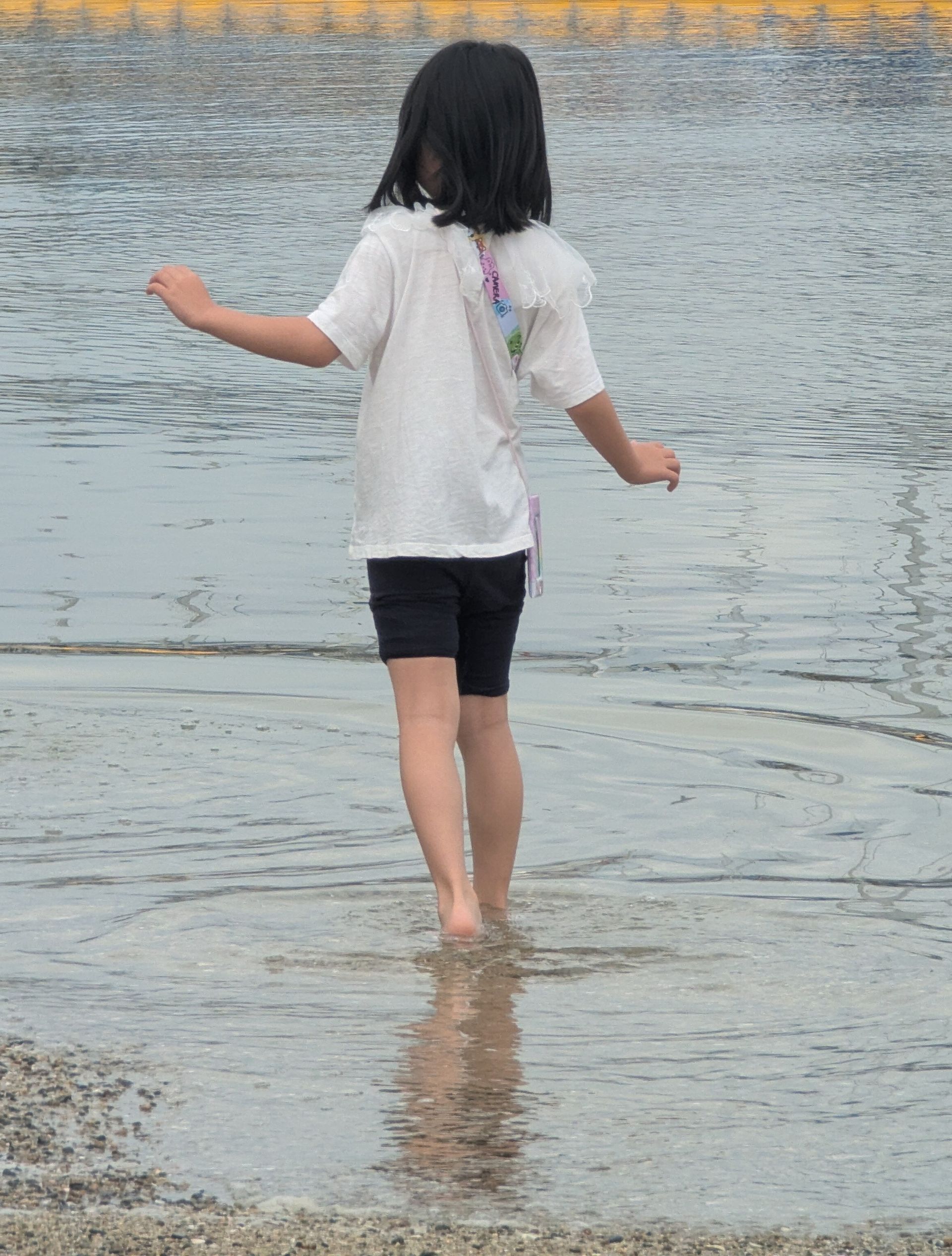 Girl wading barefoot in shallow water, wearing white shirt and black shorts.