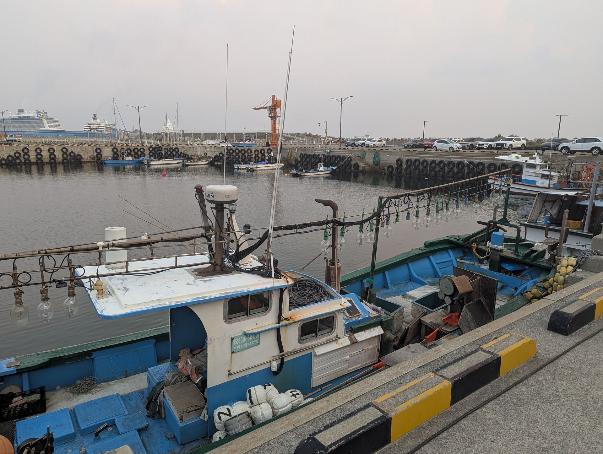 Fishing boats docked in a harbor with a blue hull and a white cabin, gray sky.