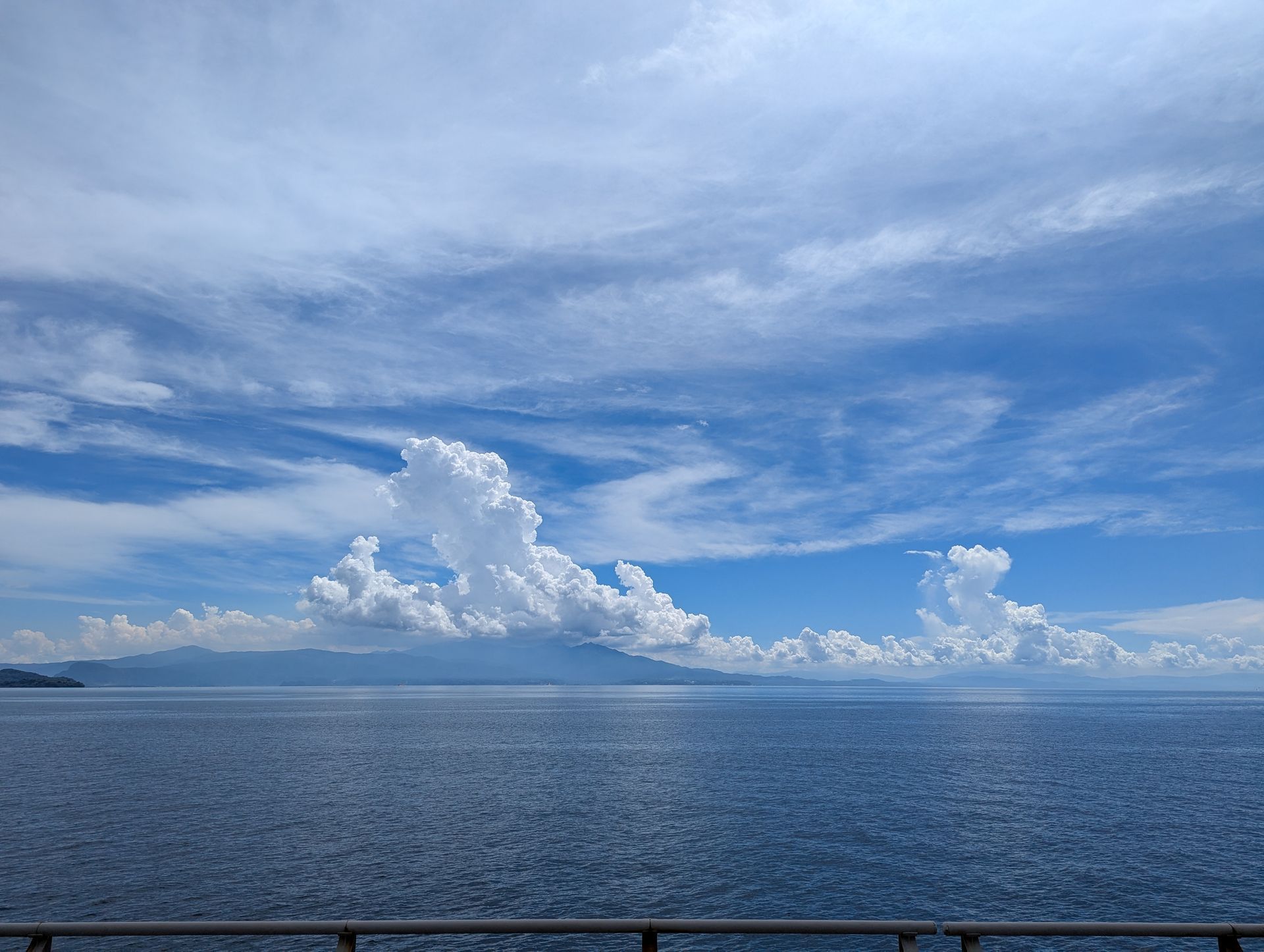 Blue ocean and sky with white puffy clouds, mountains in the distance.
