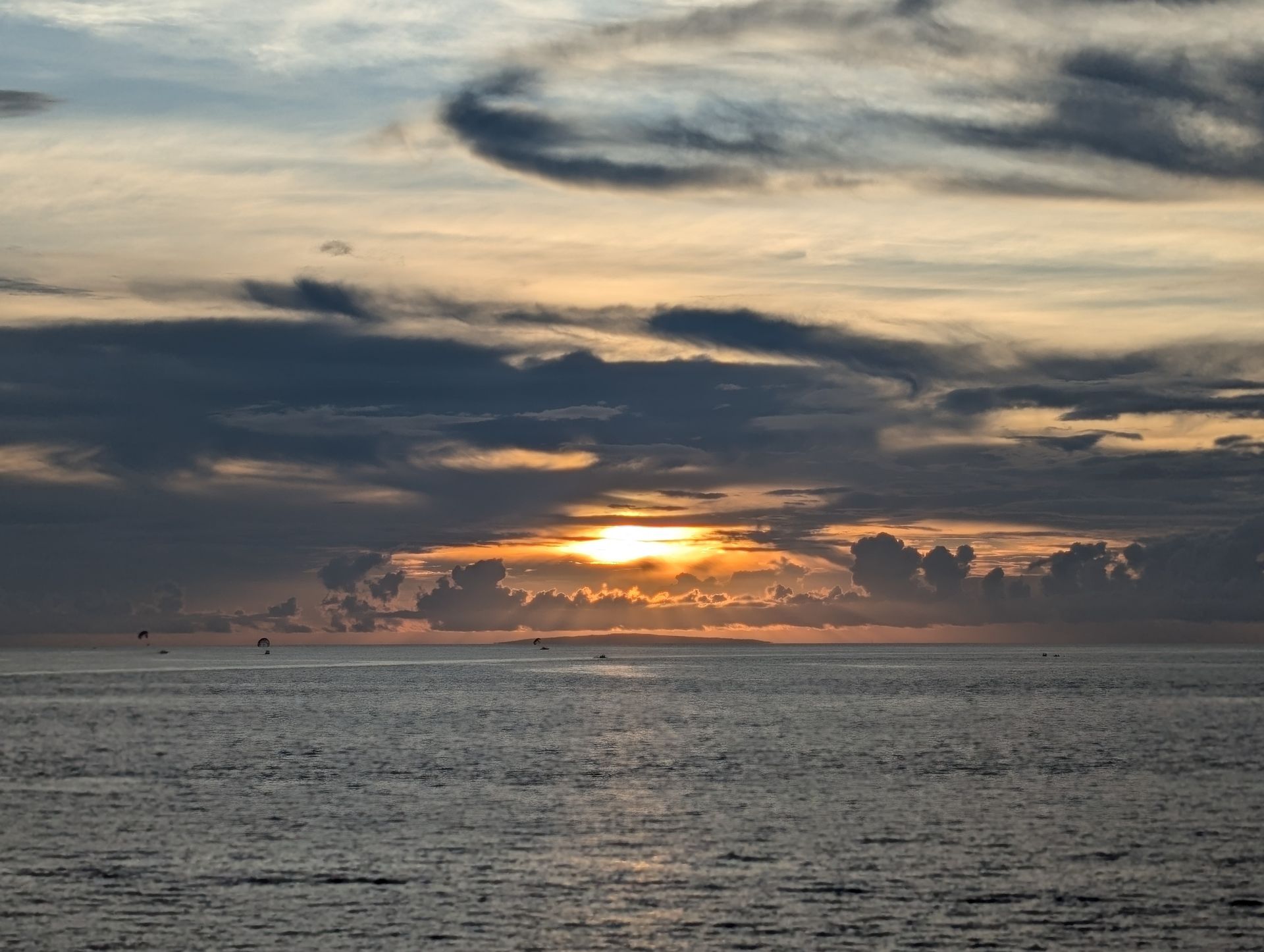 Sunset over the ocean: Sun peaking through dark clouds, creating orange and gold hues, reflecting on the water.