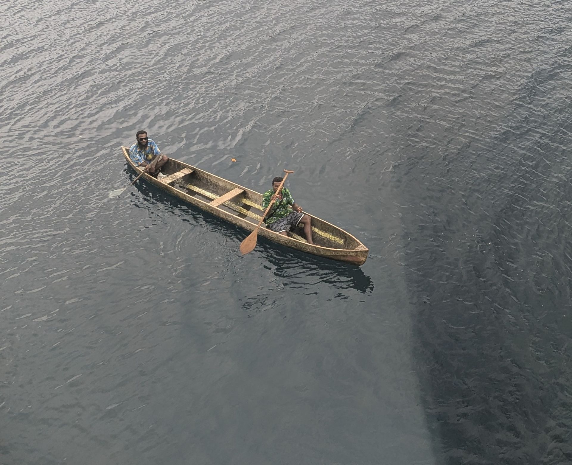 Two people paddle a wooden boat on a body of water.