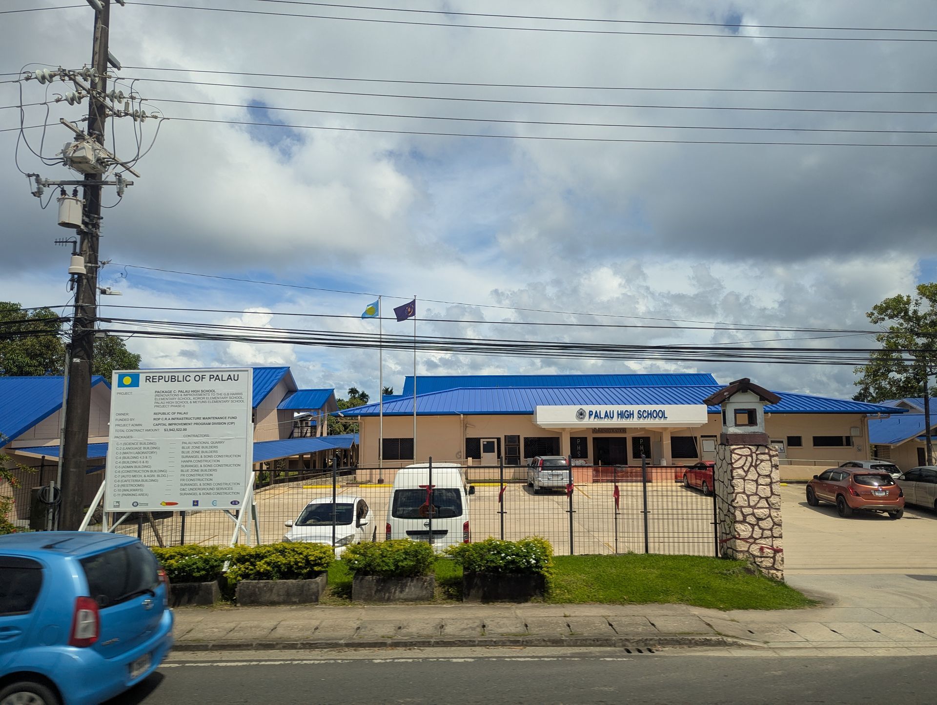 A building with a blue roof and sign, likely a hospital or clinic. Cars parked out front.