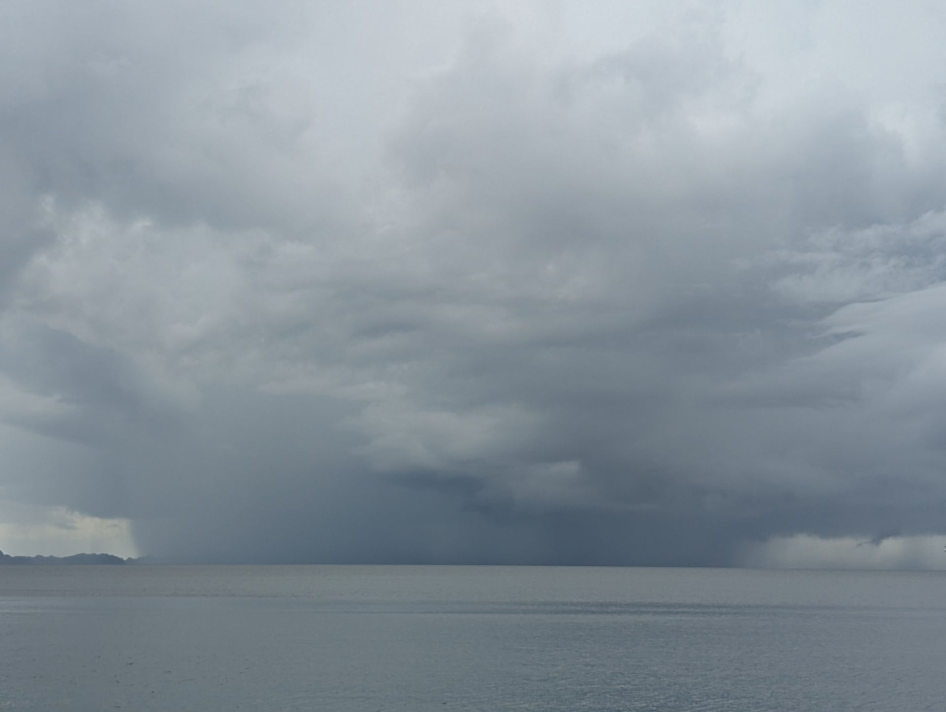 Overcast sky with heavy, dark clouds over a calm sea, and visible rain.