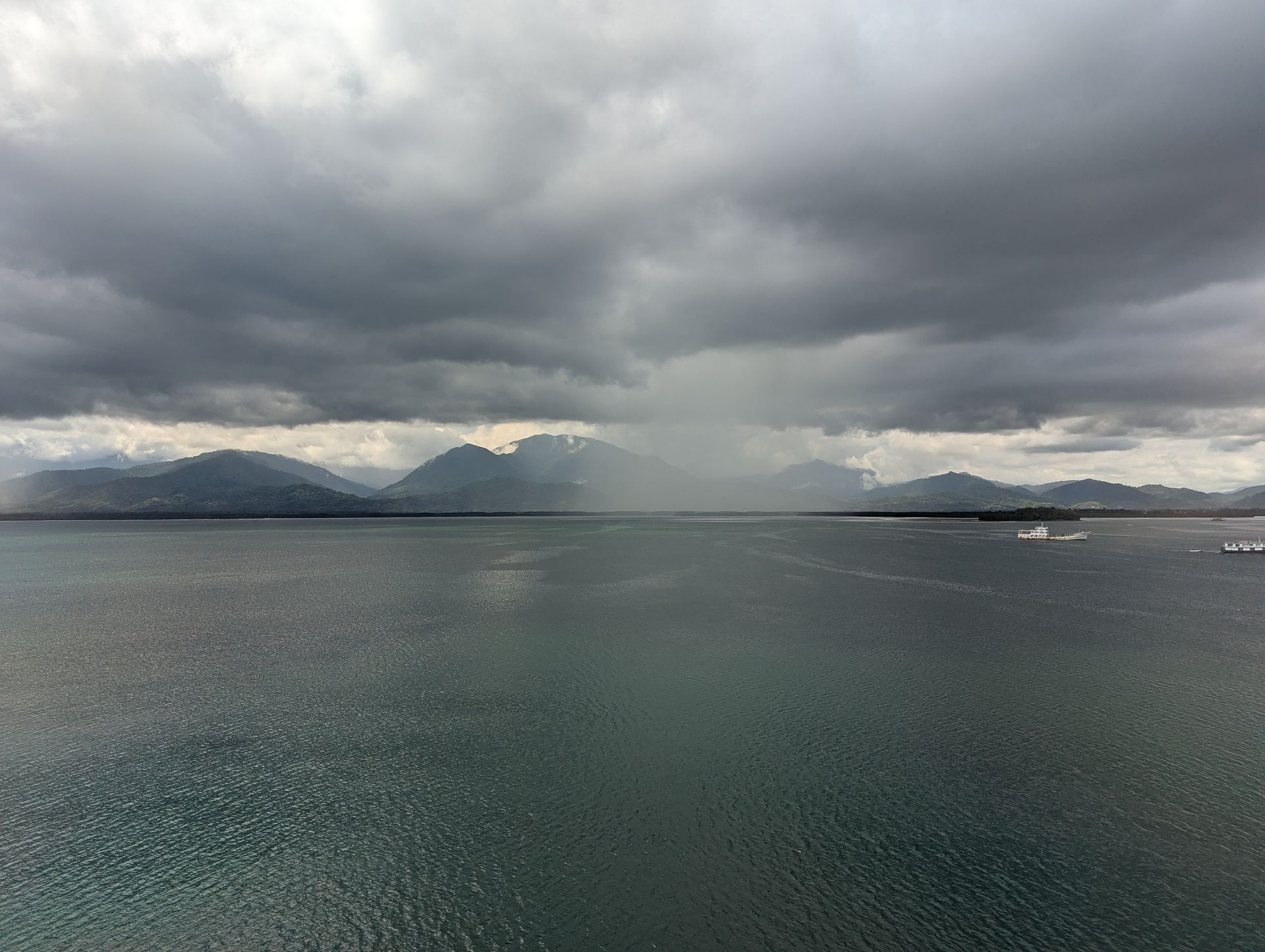 Dark, stormy sky over a body of water with mountains in the background and a ship.