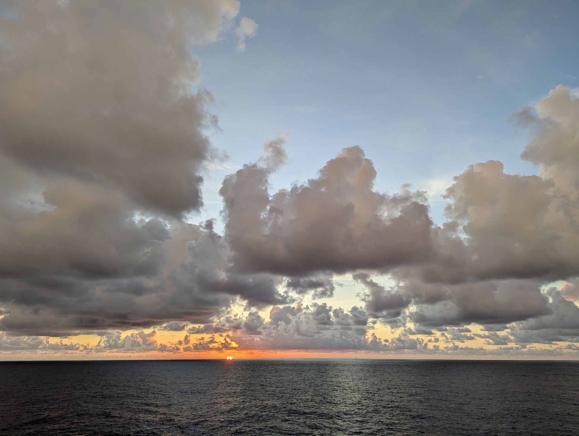 Sunset over dark ocean with cloudy sky.