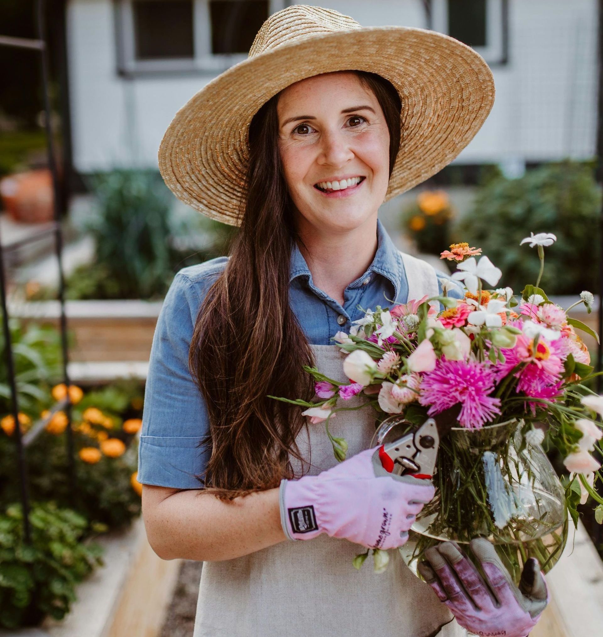 A woman wearing a straw hat and pink gloves is holding a vase of flowers.