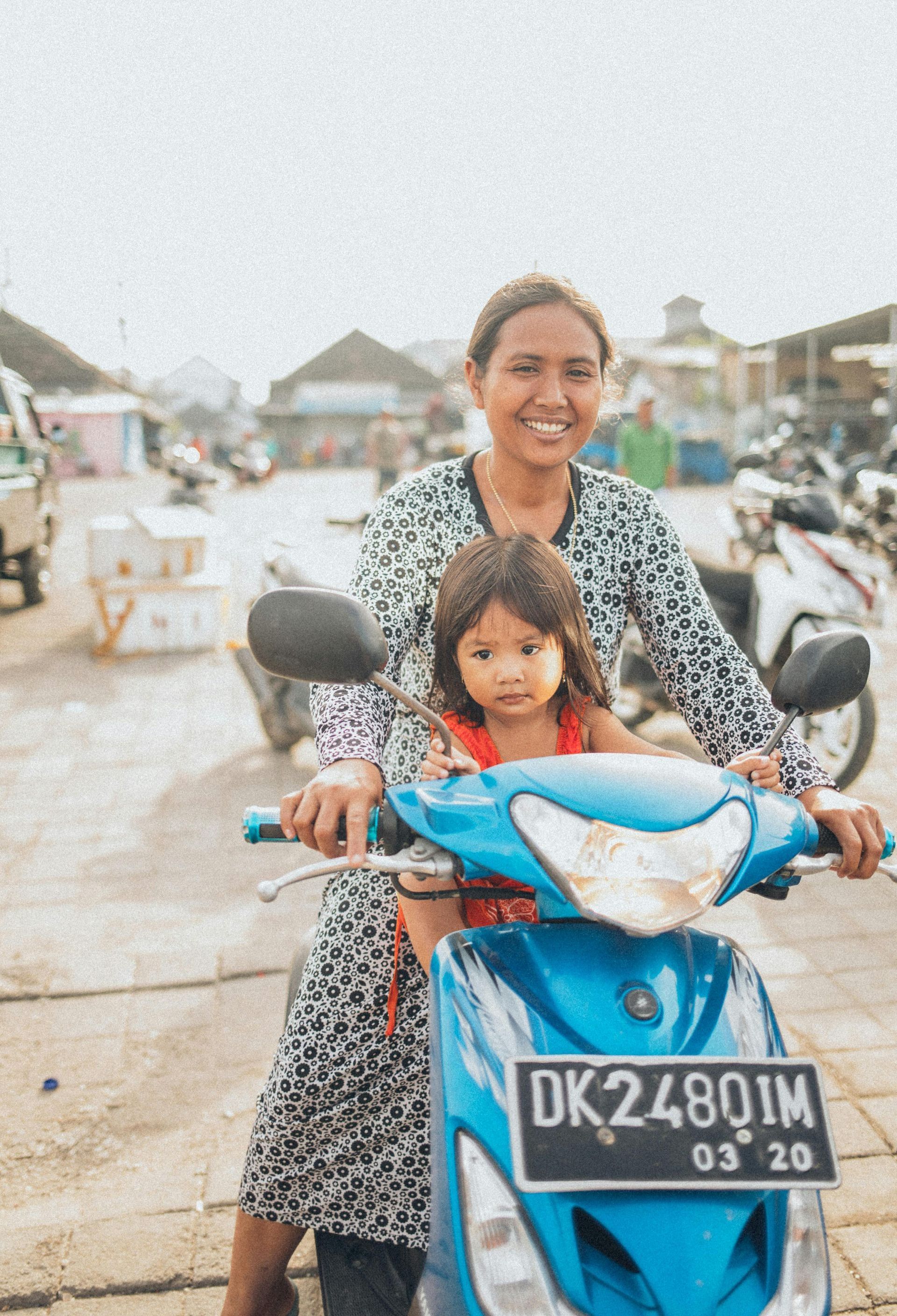 A woman is riding a blue scooter with a little girl on the back.