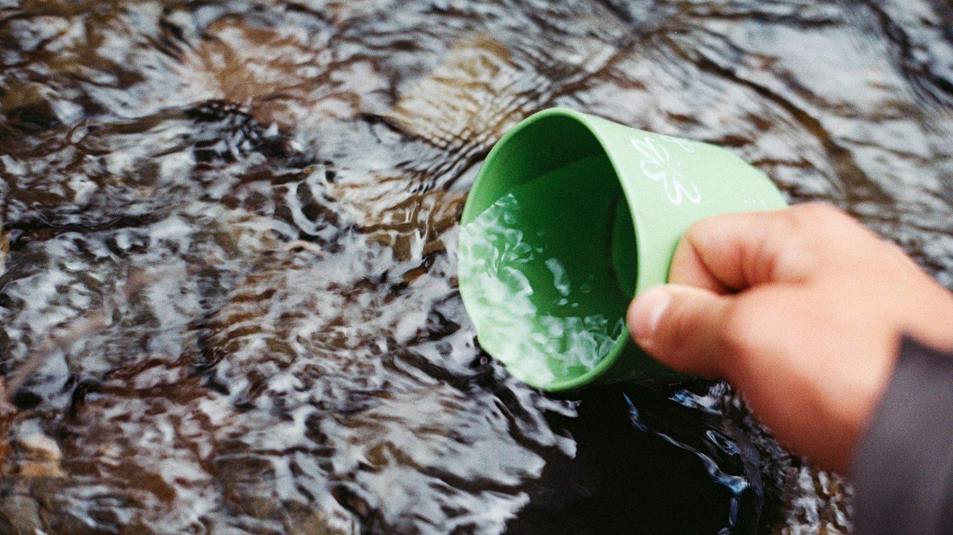 A person is pouring water from a green cup into a stream.