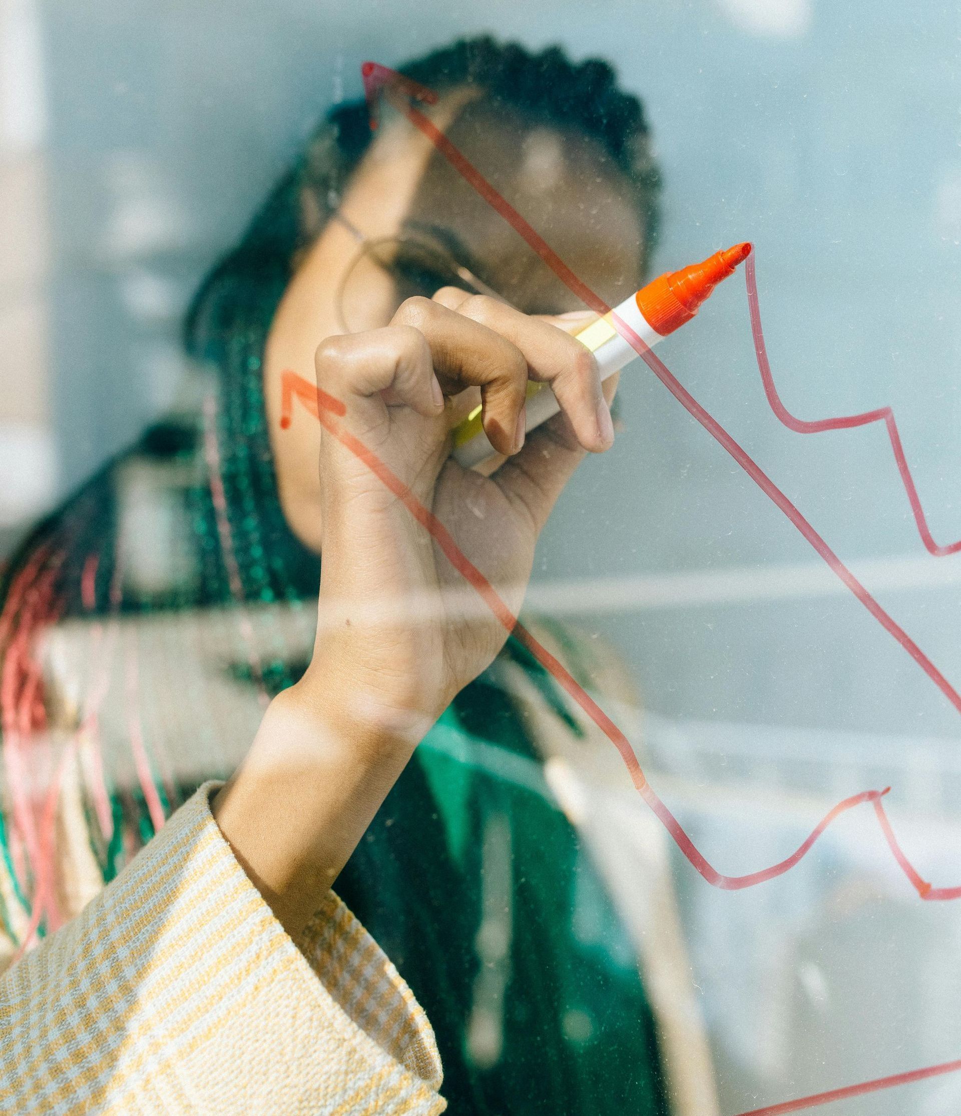 A woman is drawing a graph on a glass wall with a marker.