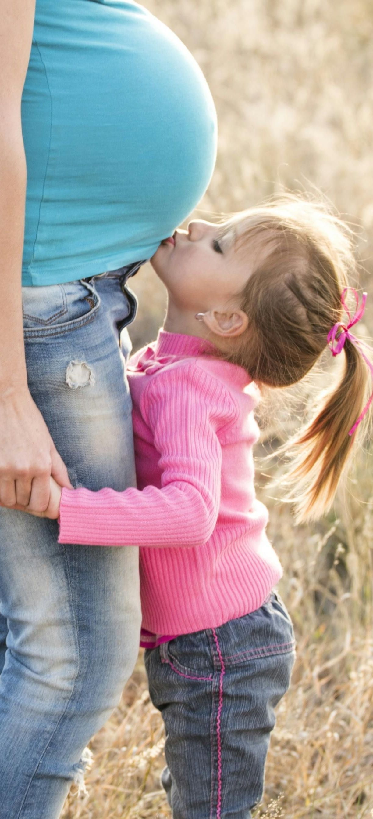 pregnant woman with a little girl kissing her belly