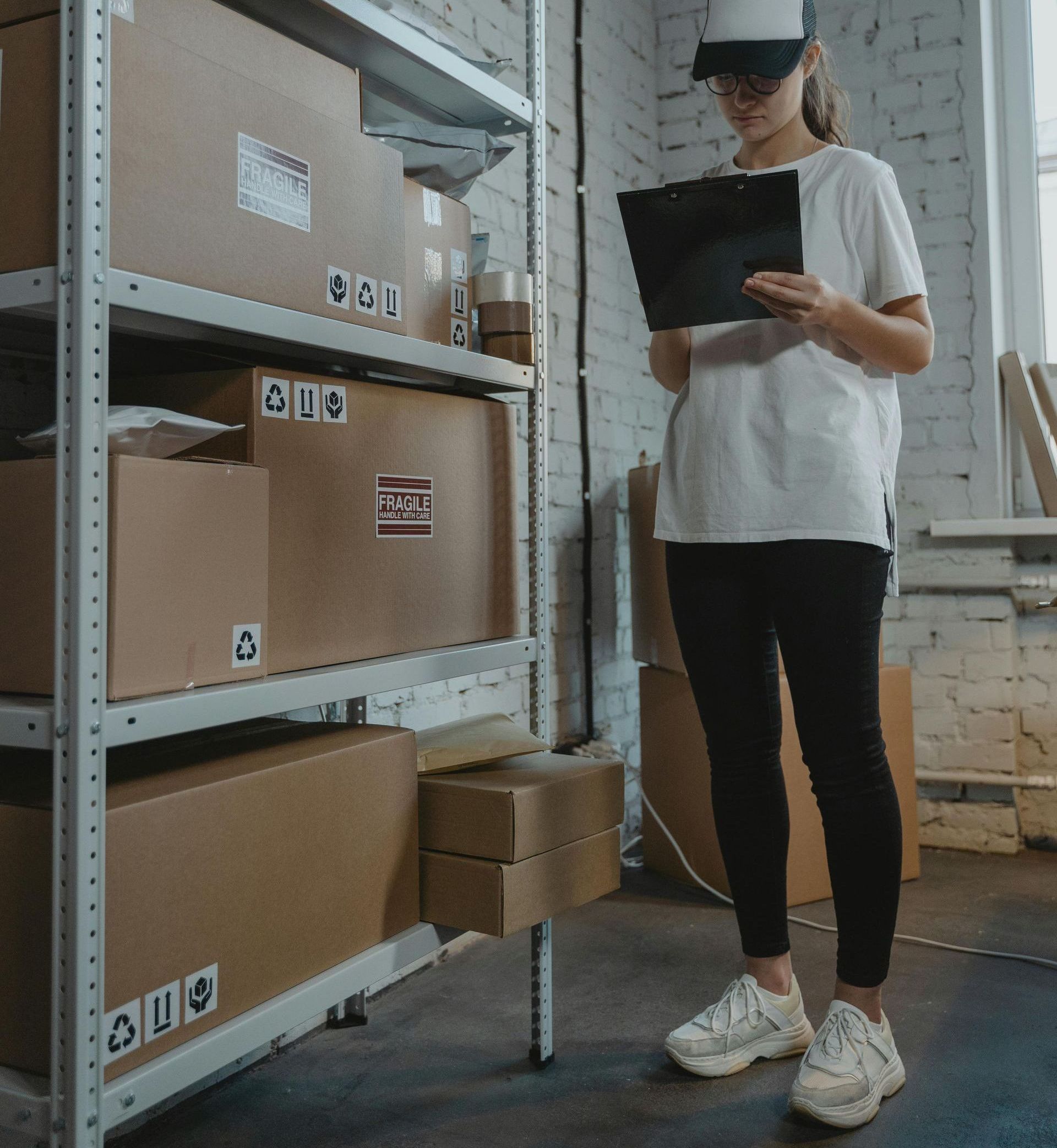 A woman is standing in a warehouse looking at a clipboard.