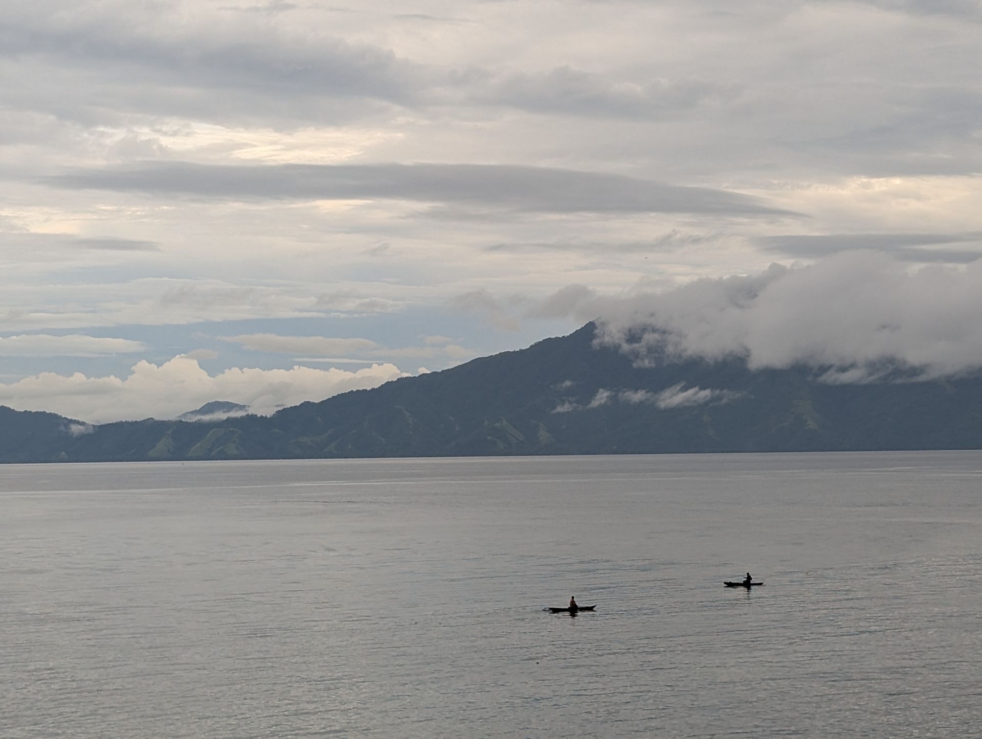 Two kayaks on a calm lake, with mountains and cloudy sky in the background.