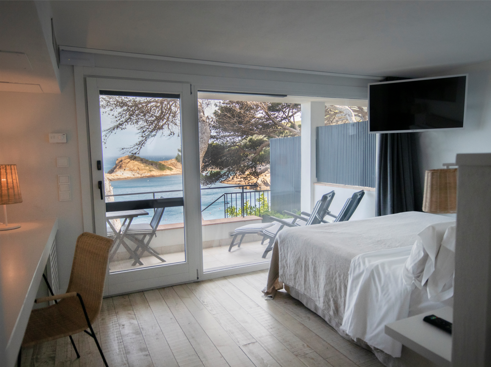 A hotel room with a bed , television , chairs and a balcony overlooking the ocean.