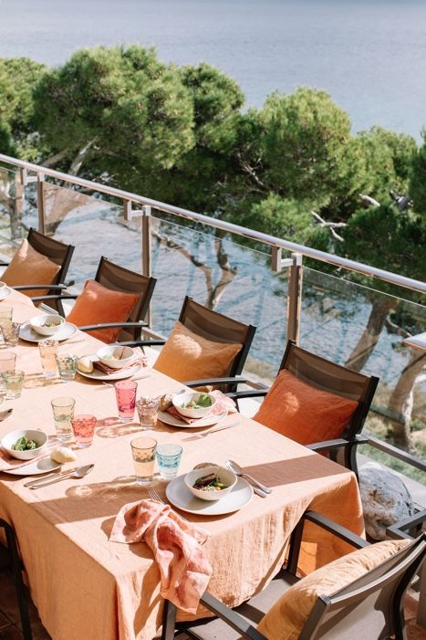 A table set for a dinner party on a balcony overlooking the ocean.