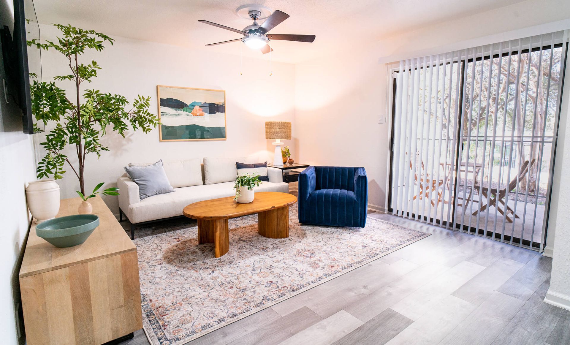 Bright living room with white sofa, blue armchair, wood coffee table, and balcony doors.
