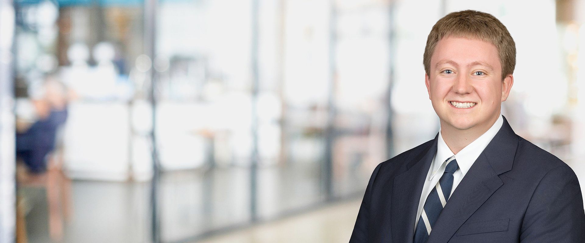 Man in suit smiling in a blurred office setting.