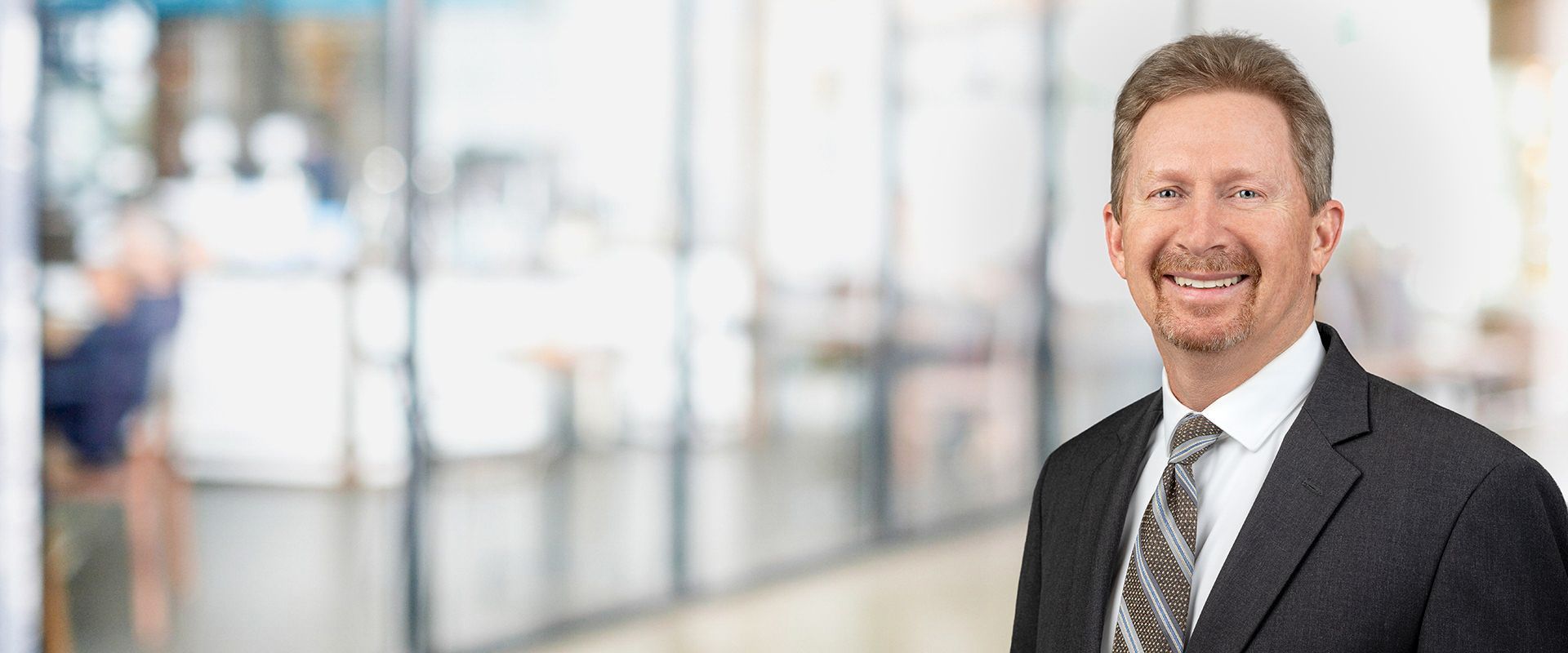 Man in a suit smiles in an office setting.