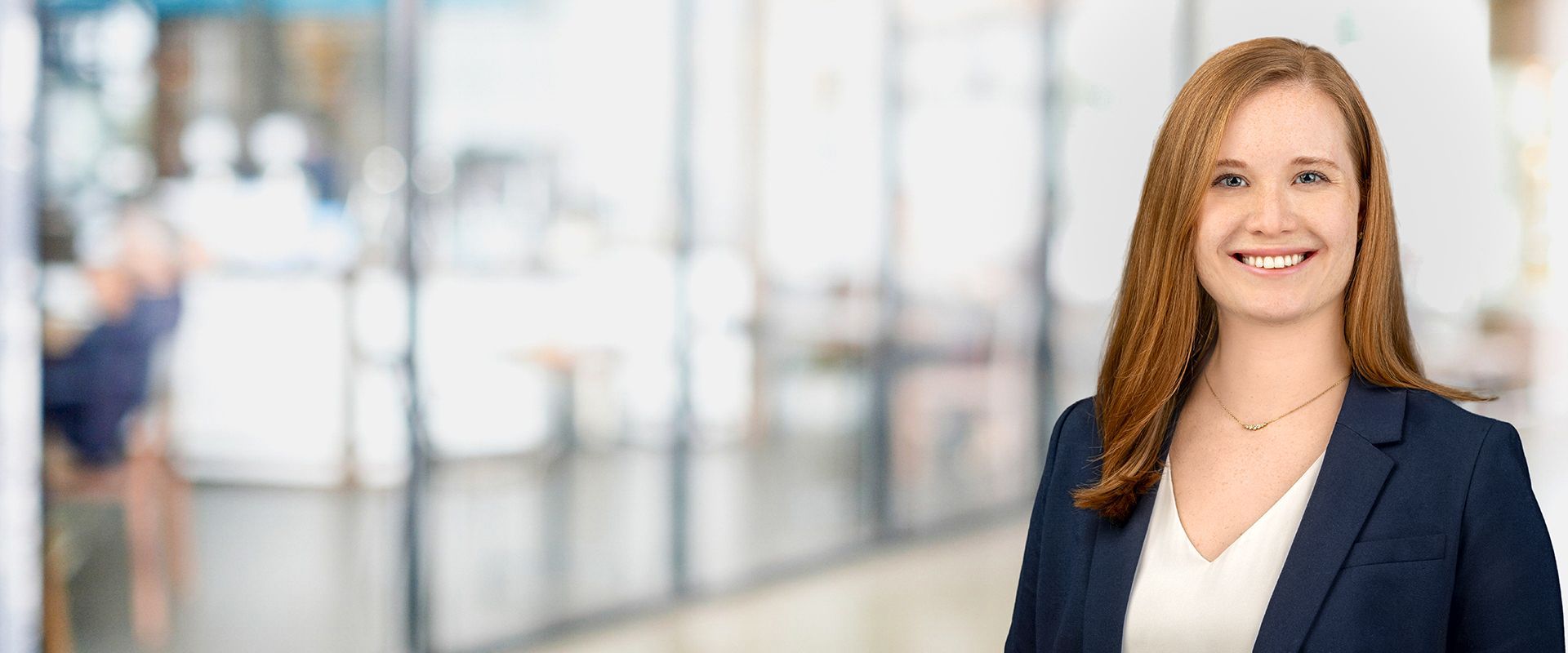 Woman in a blue blazer smiles at the camera in a modern office setting.