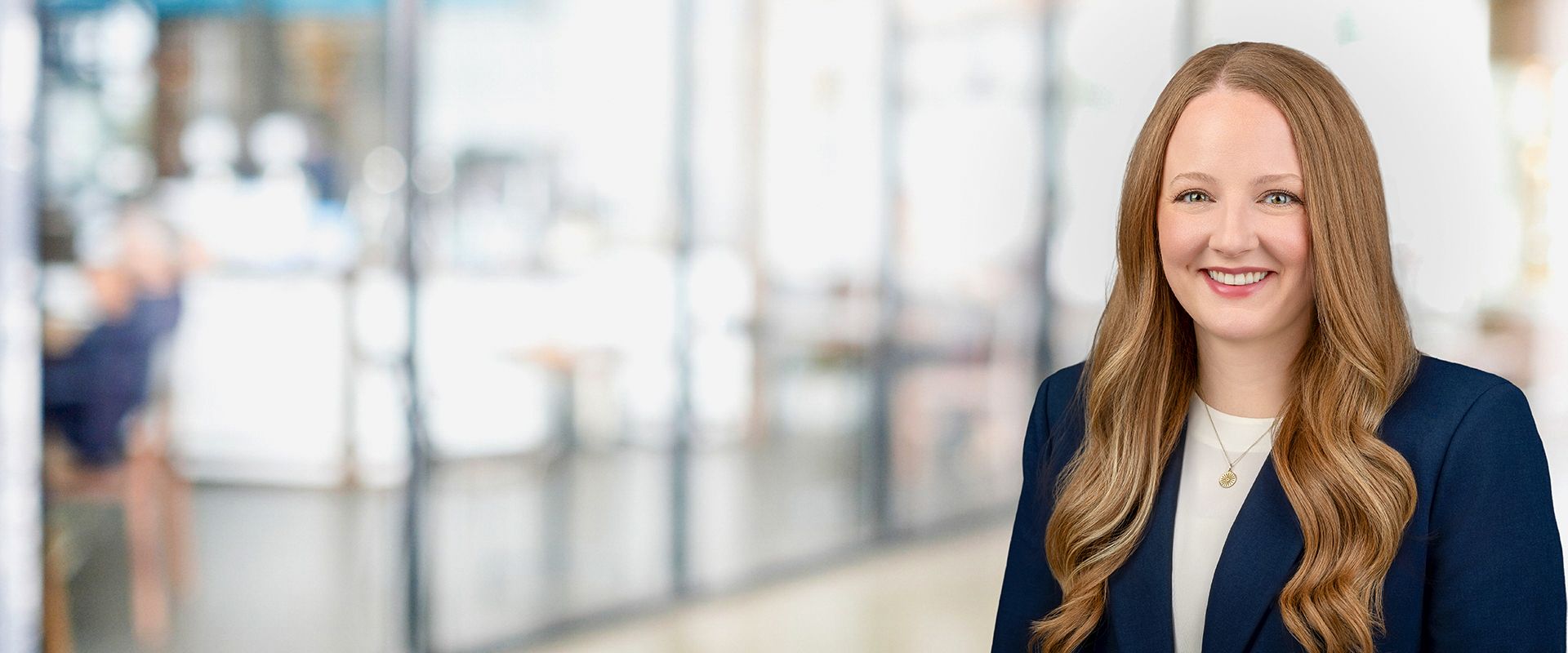 Woman in a blue blazer smiles in an office setting.