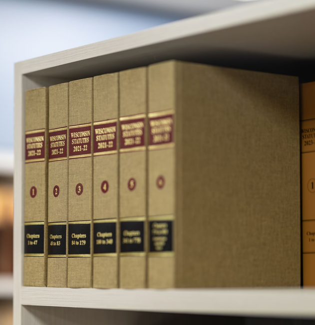 Books on a shelf with gold spines and red labels, in a library or office setting.