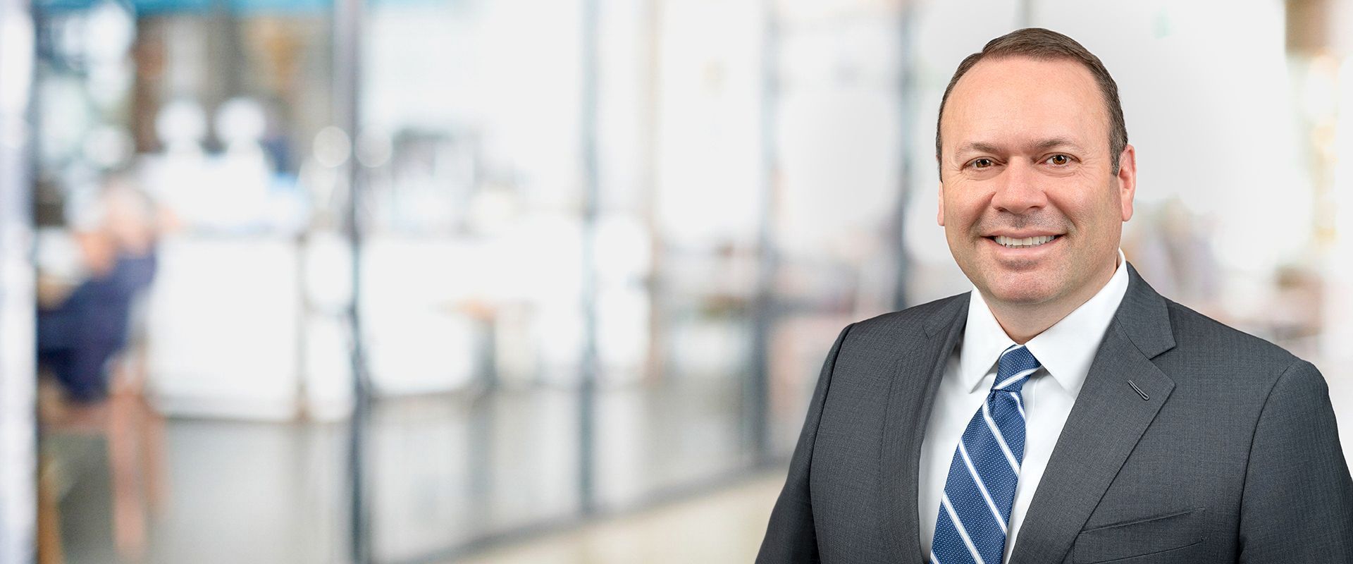 Man in suit smiling in a blurred office setting.