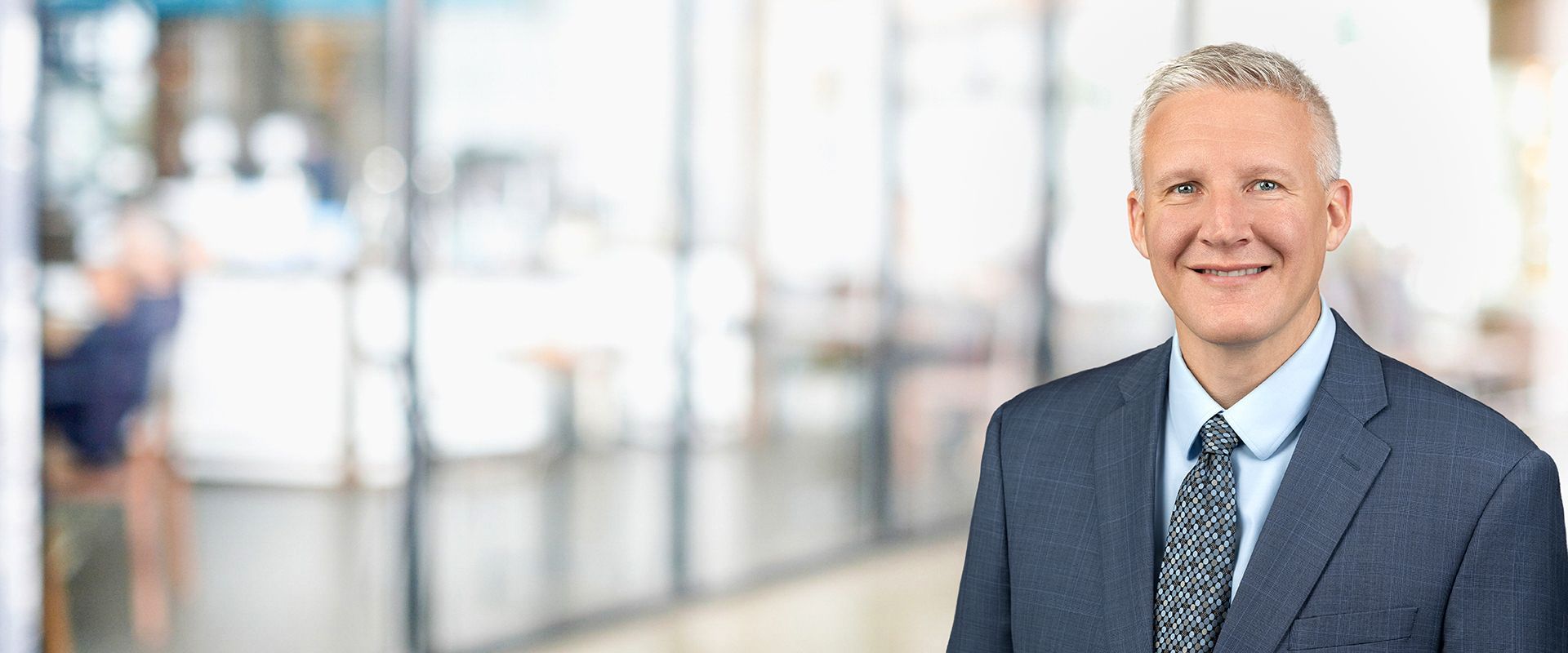 Man in suit smiles in a blurred office background.