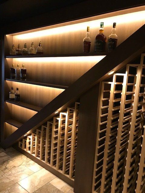 A wine cellar under a staircase with bottles on shelves