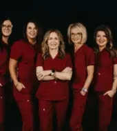 Six professionals in maroon scrubs stand together against a black background, posing for a group portrait.