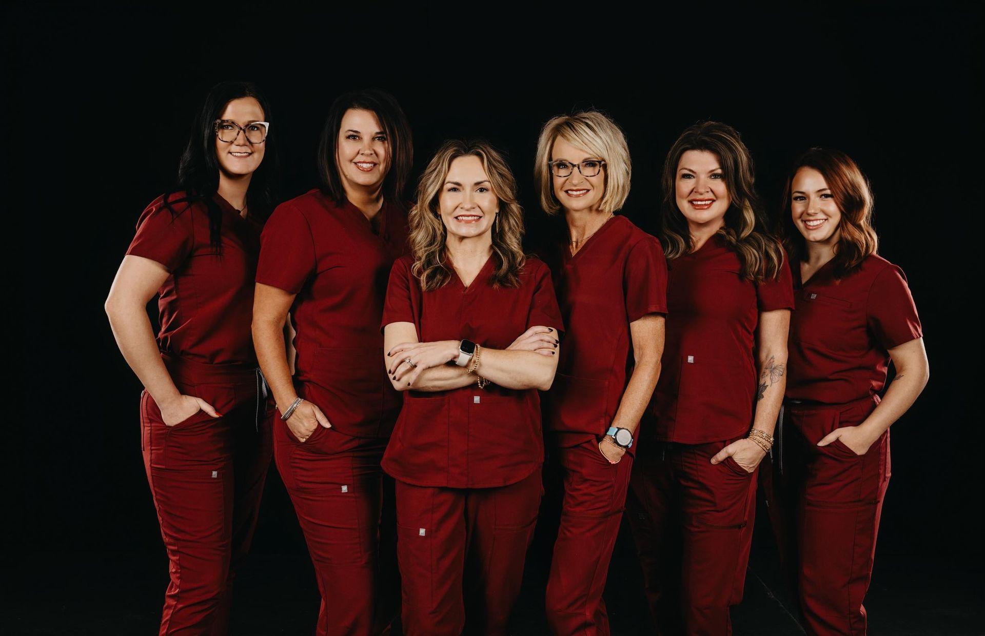 Six professionals in maroon scrubs stand together against a black background, posing for a group portrait.