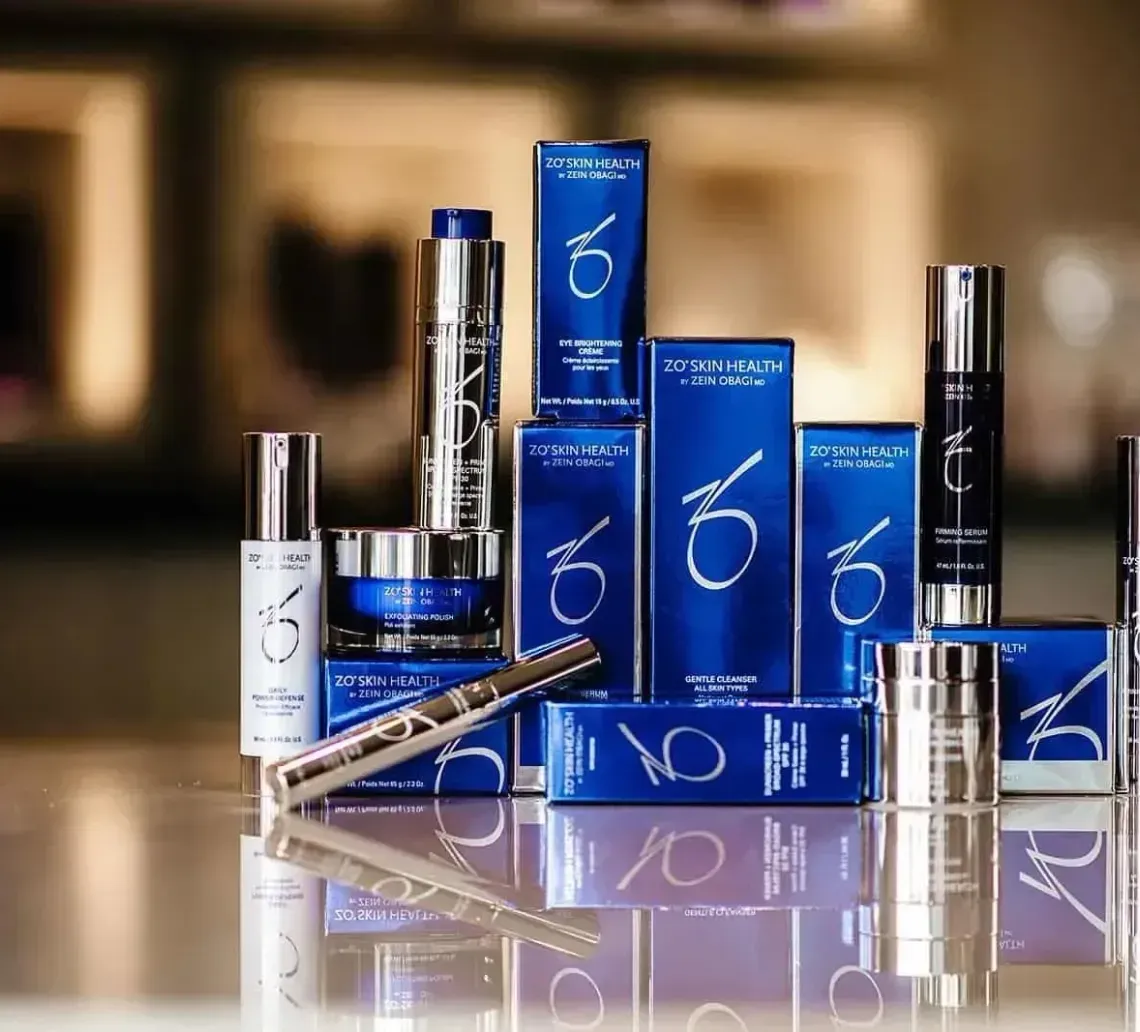 A collection of ZO Skin Health skincare products in blue packaging displayed on a reflective surface.