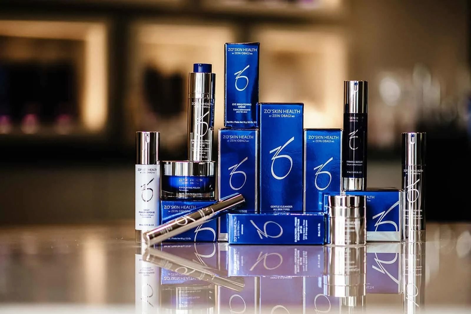 A collection of blue and silver ZO Skin Health skincare products arranged on a reflective surface.