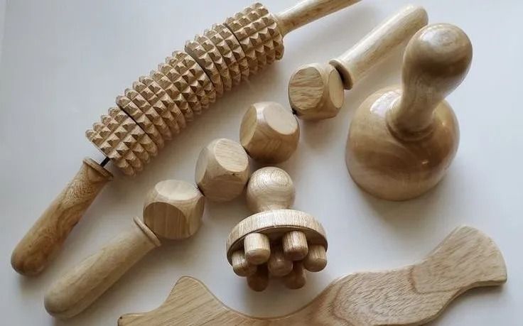 A set of various wooden massage tools for maderotherapy, including rollers, a bell-shaped cup, and a contoured board.