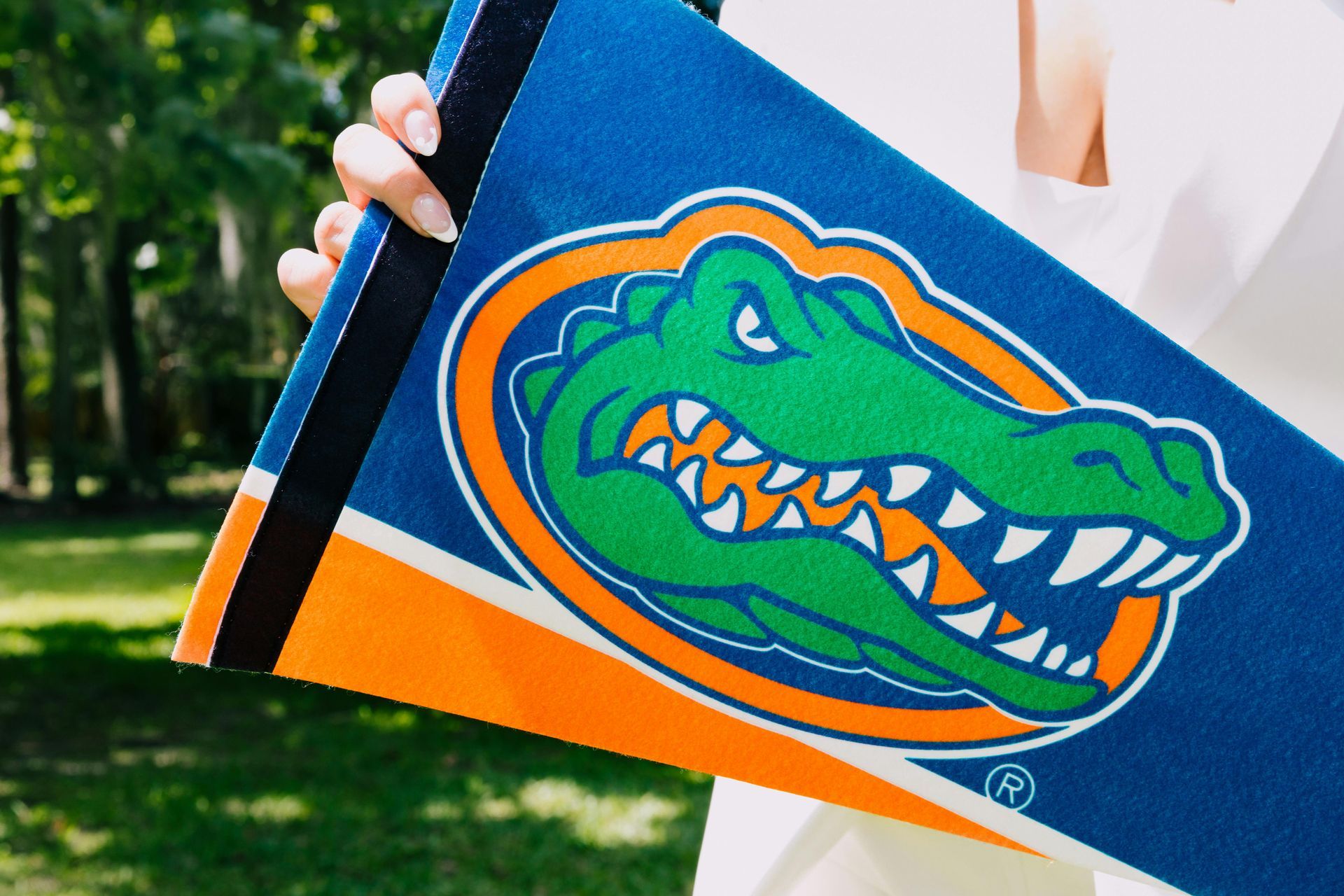 Person holds a University of Florida Gators banner. Blue and orange colors. Outdoor setting.