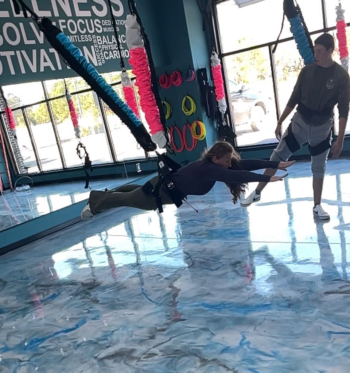 A man and a woman are doing aerial yoga in a gym.
