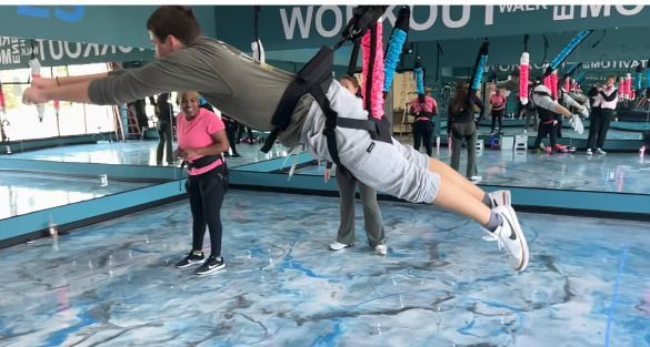 A man is flying through the air in a gym while wearing a harness.