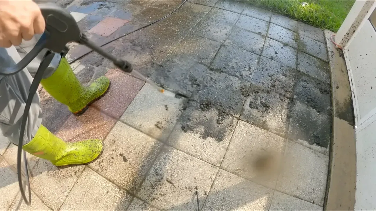 Person power washing a stone patio, wearing green boots.