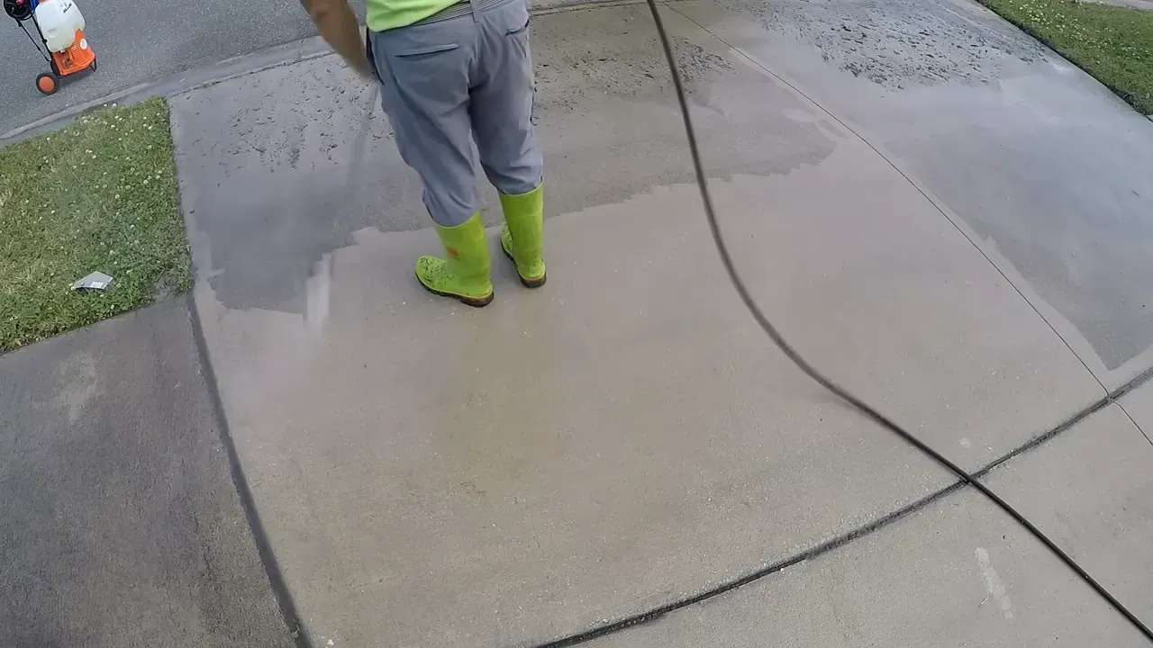 Person power washing a concrete sidewalk, wearing green boots.