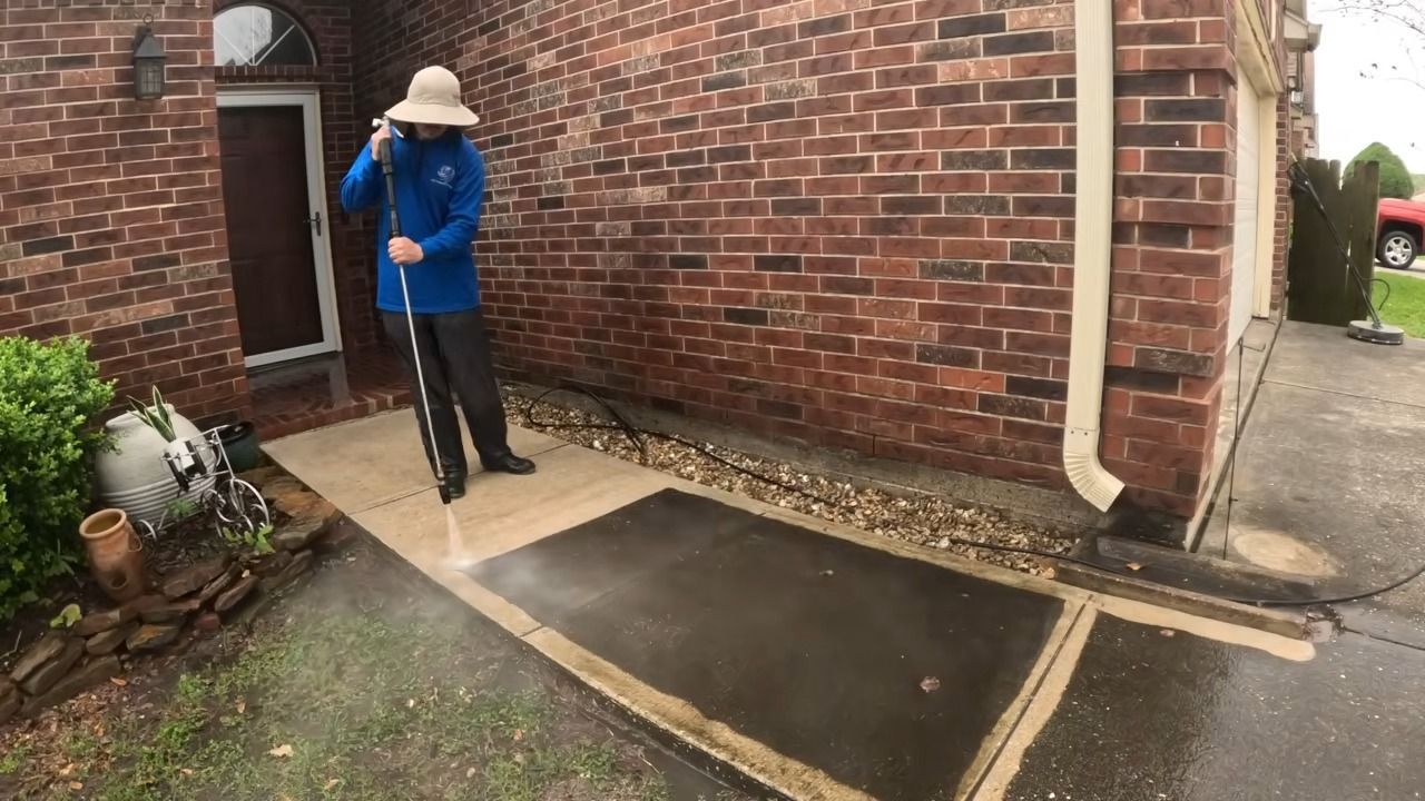 Person pressure washing a concrete walkway next to a brick building.