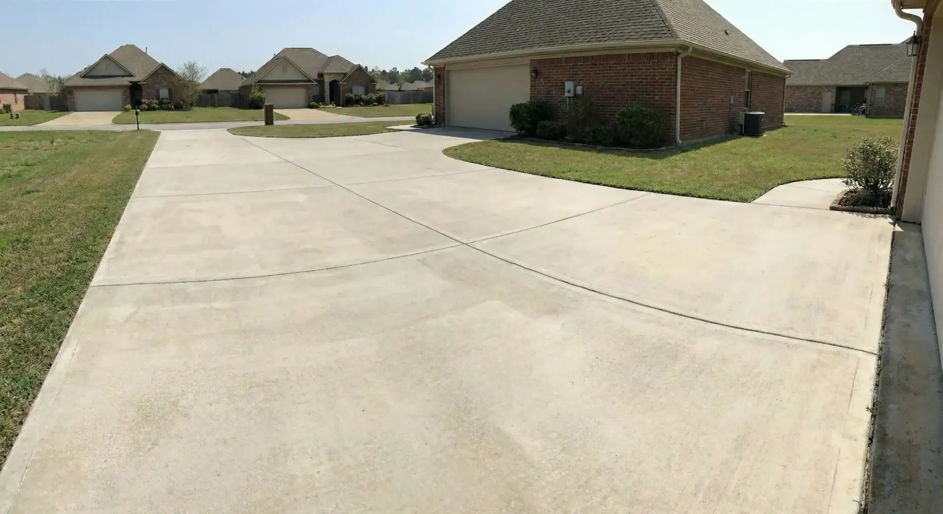Concrete driveway in a suburban neighborhood, leading to a house with a garage and green lawn.